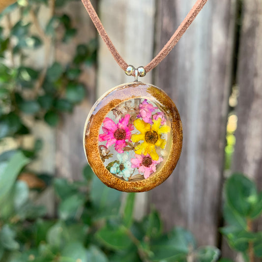 Round pendant with pressed flowers on a brown cord against a natural background